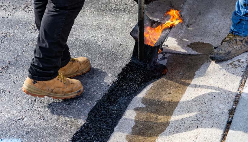 Trabalhador aplicando asfalto quente em reparo de via